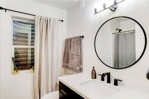 Bathroom features a sleek vanity, round mirror, and towel rack.