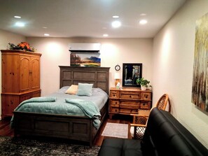 A bedroom with a bed, dresser, chair, and artwork on the wall.