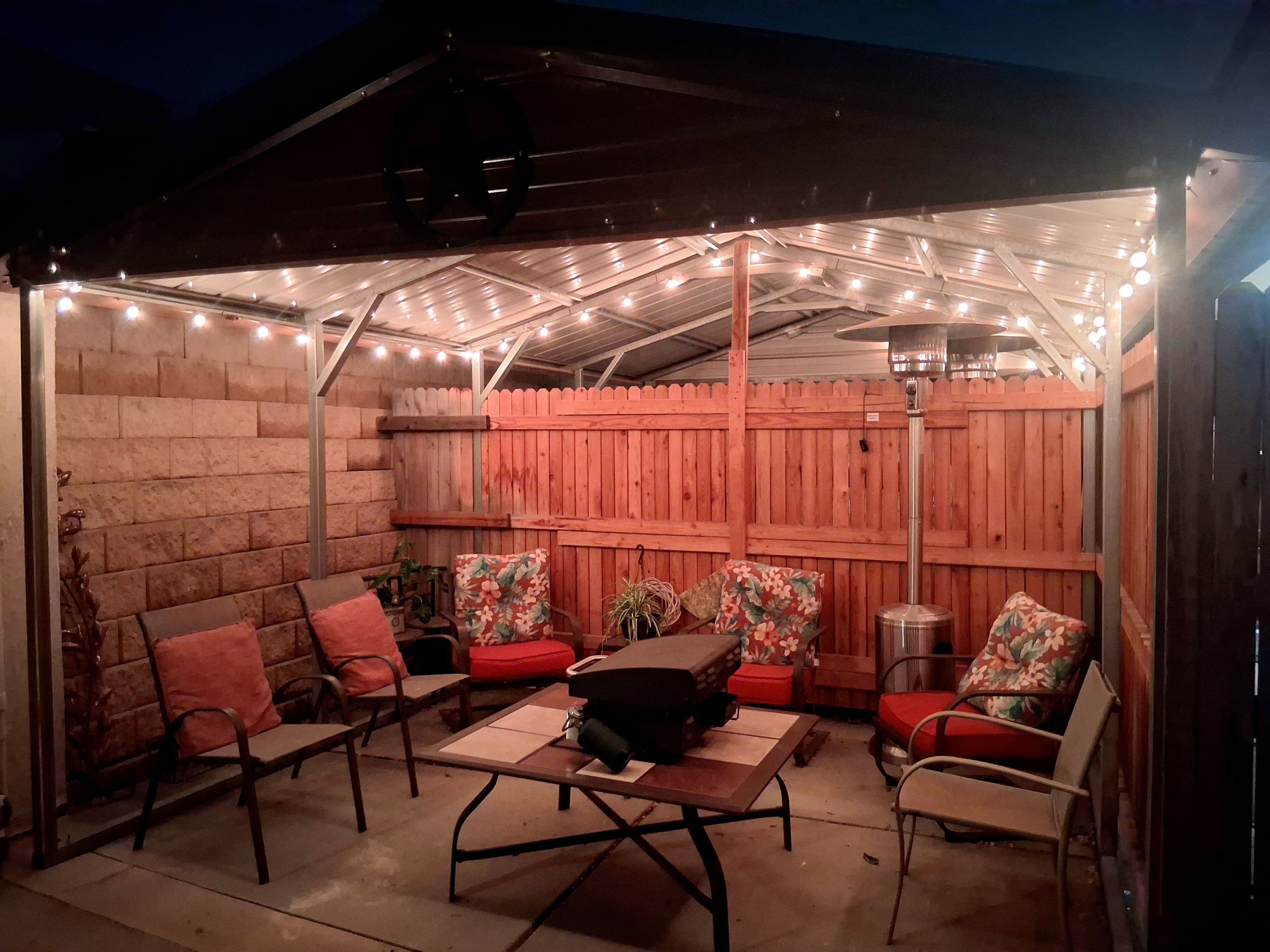 An outdoor patio with a covered seating area, string lights, and a wooden fence.