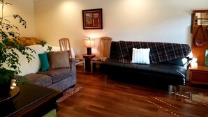 Ein Wohnzimmer mit einer Couch, Sesseln, einer Lampe, einer Pflanze und einem gerahmten Bild an der Wand.