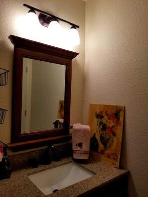 Un baño con un espejo grande, un lavabo y un cuadro en la pared.