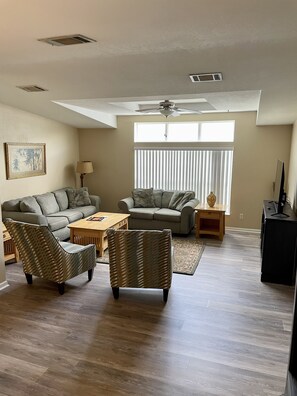 Relax in this spacious living room with a high ceiling, ceiling fan, and large window.