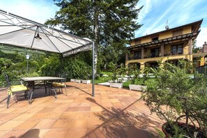 Een terras met een tafel en stoelen, een overdekt gedeelte en een gebouw met balkons.