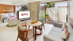 En moderne stue med et fjernsyn der viser 'NETFLIX', en sofa, et spisebord med stole og udsigt til en have gennem en skydedør.