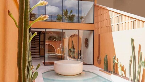 Een modern binnenzwembad met een bubbelbad, omgeven door cactussen en planten, met een glazen wand die uitzicht biedt op een gebouw met een balkon.