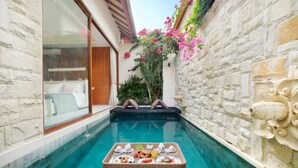 A narrow pool with a dining table set for two, surrounded by stone walls and a wooden door. - Glamour 1BR Private Villa Kuta (Bali)
