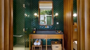 Ein Badezimmer mit Glasdusche, einem hölzernen Waschtisch mit Spiegel und einer Wand mit grünen Fliesen.