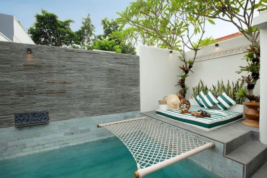 A pool area with a netted lounging area, a stone wall, and a seating area with cushions and plants.