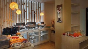 Un espace buffet proposant divers plats, une machine à café et un présentoir de fruits.