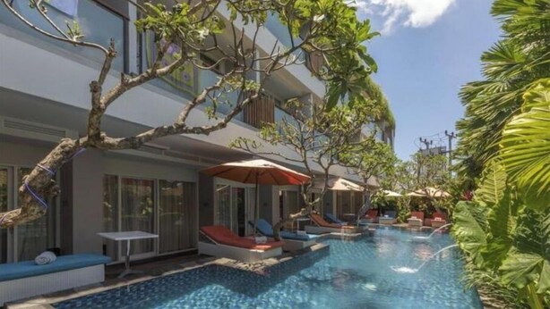 Une piscine entourée d’arbres et d’un bâtiment, avec des chaises longues et des parasols.
