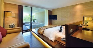 A modern hotel room with a large bed, a sofa, a desk, and a TV. - Whirlpool Suite Room In Seminyak (Bali)