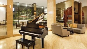 A grand piano in a spacious lobby with a modern interior, large windows, and a seating area with sofas and a coffee table. - Whirlpool Suite Room In Seminyak (Bali)