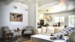 Un salon avec un canapé blanc, deux fauteuils, une table basse et une œuvre d’art représentant une carte du monde accrochée au mur.