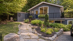 Une maison avec un chemin de pierre menant à la porte d’entrée, entourée de verdure et d’une clôture.