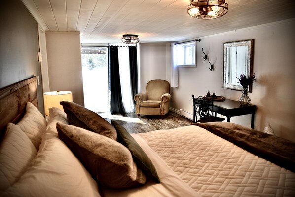 A bedroom with a large bed, a chair, a desk, and a window.