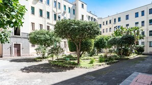 Une cour intérieure agrémentée d’arbres, un chemin pavé et un bâtiment doté de nombreuses fenêtres.