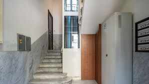 Un escalier menant à une porte, un coffret électrique et un réfrigérateur.