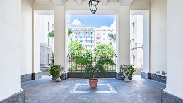 Un espace extérieur abrité, agrémenté d’un grand pot de fleurs au centre, d’une rambarde en métal et offrant une vue sur les bâtiments en arrière-plan.