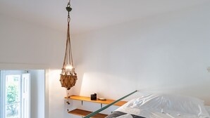 Une chambre à coucher avec un lit, un luminaire suspendu, une étagère en bois et une fenêtre.