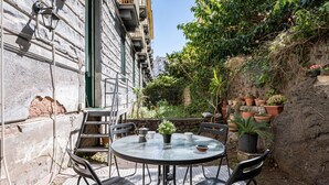 Une table ronde d’extérieur, entourée de chaises, de plantes en pot et d’un mur de pierre.