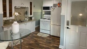 Een moderne keuken met witte kasten, een glazen eettafel en een roestvrijstalen koelkast.