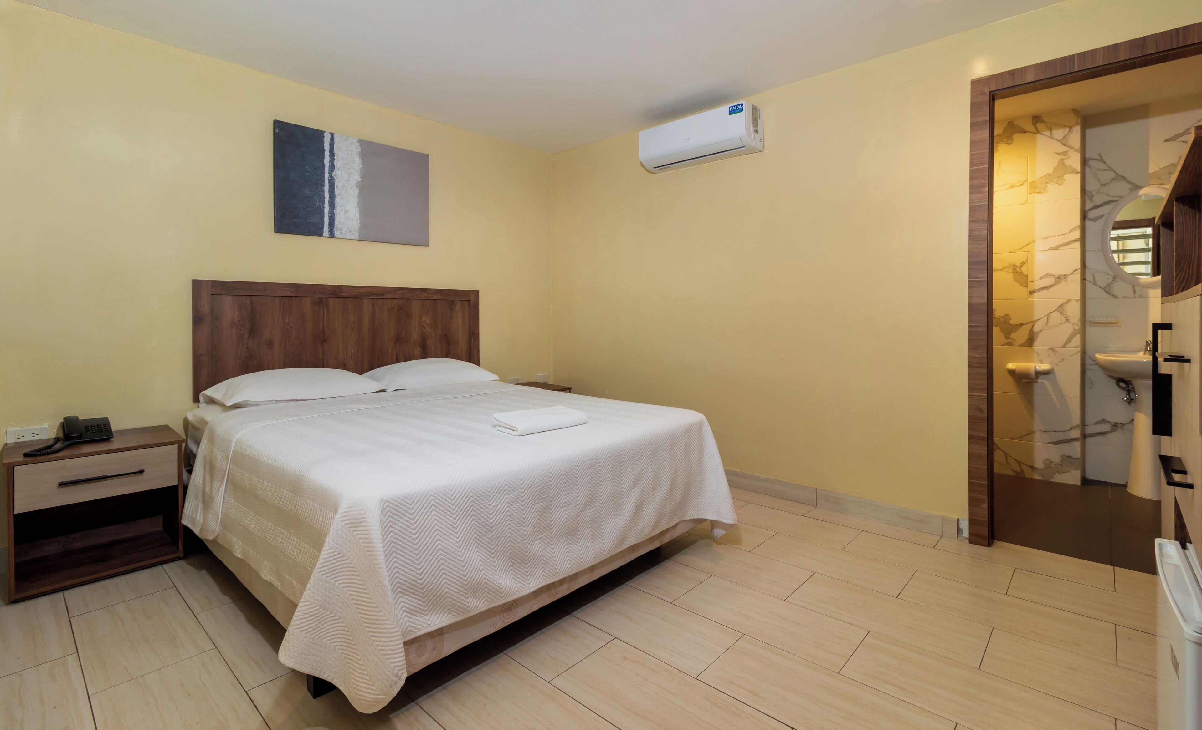 A hotel room with a bed, bedside table, and an air conditioning unit.