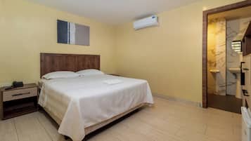 A hotel room with a bed, bedside table, and an air conditioning unit.