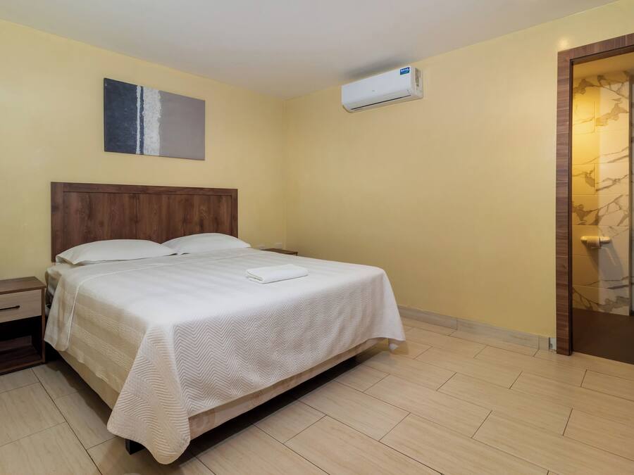A hotel room with a bed, bedside table, and an air conditioning unit.