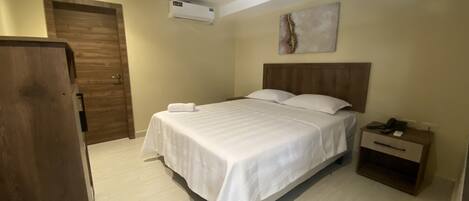 Una habitación de hotel con cama, mesita de noche y una puerta.