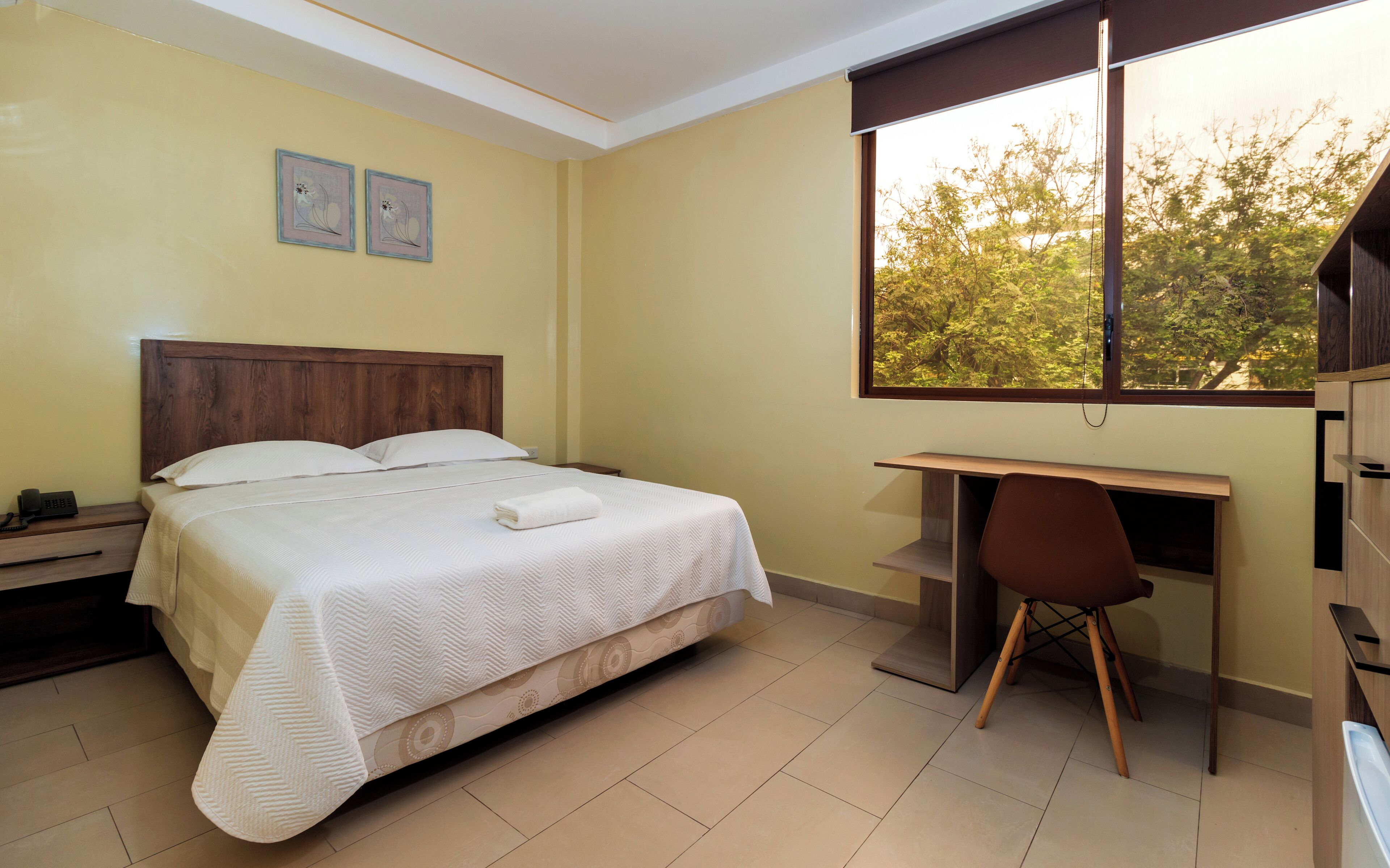 A bedroom with a bed, a desk, and a chair. There is a window with a view of trees.