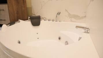 Ett stort, ovalt badkar med ett svart handfat, ett duschmunstycke och en massageapparat som man kan hålla i handen.