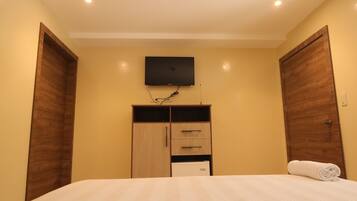 Une chambre à coucher avec un lit, un téléviseur fixé au mur, des armoires en bois et un radiateur blanc.