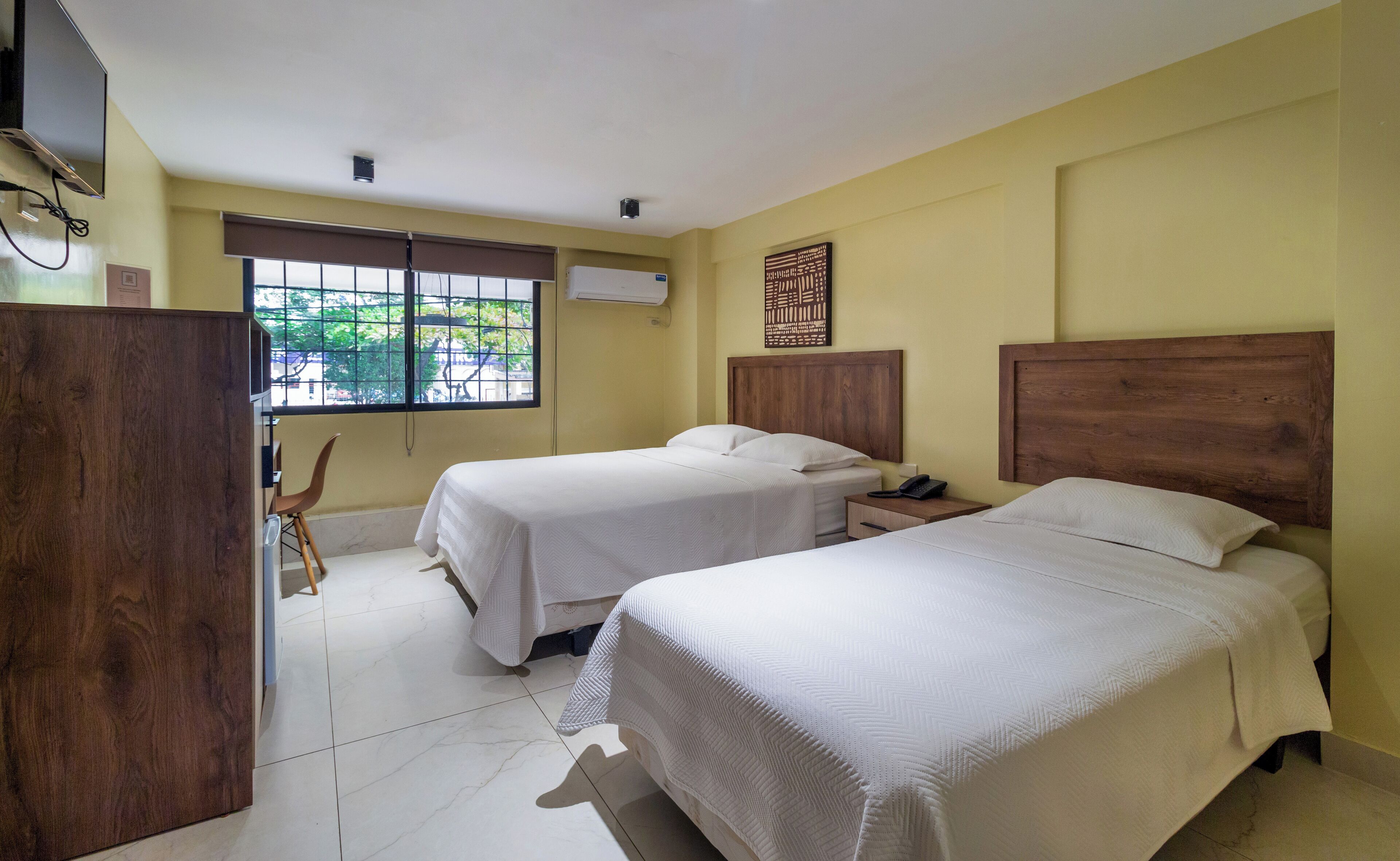 Quarto de hotel com duas camas, uma mesa, uma cadeira e janela com vista.