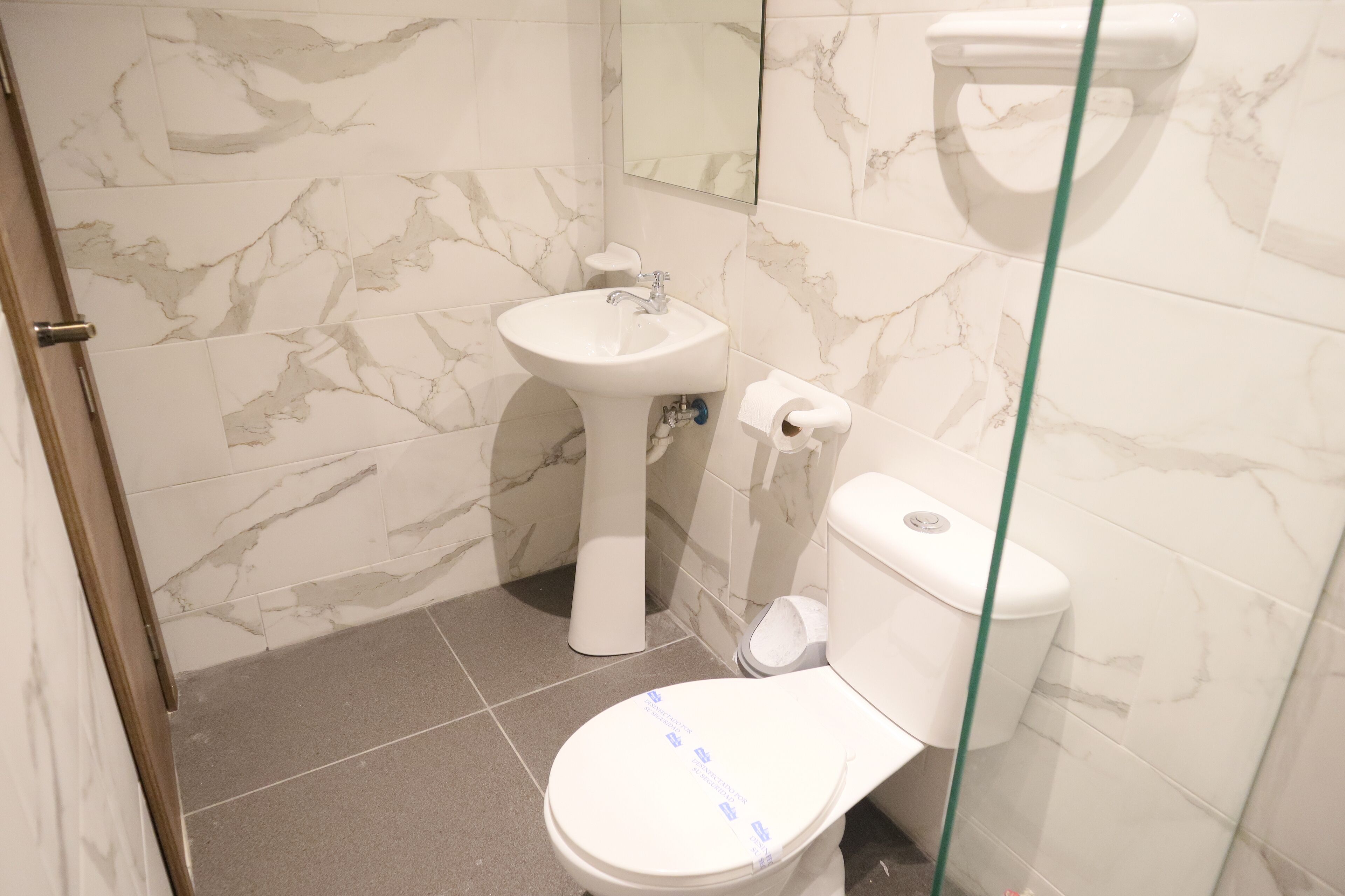 A bathroom with a toilet, sink, and marble-tiled walls.