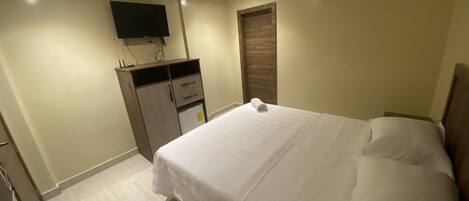 A bedroom with a bed, a wardrobe, a flat-screen TV mounted on the wall, and an air conditioning unit.