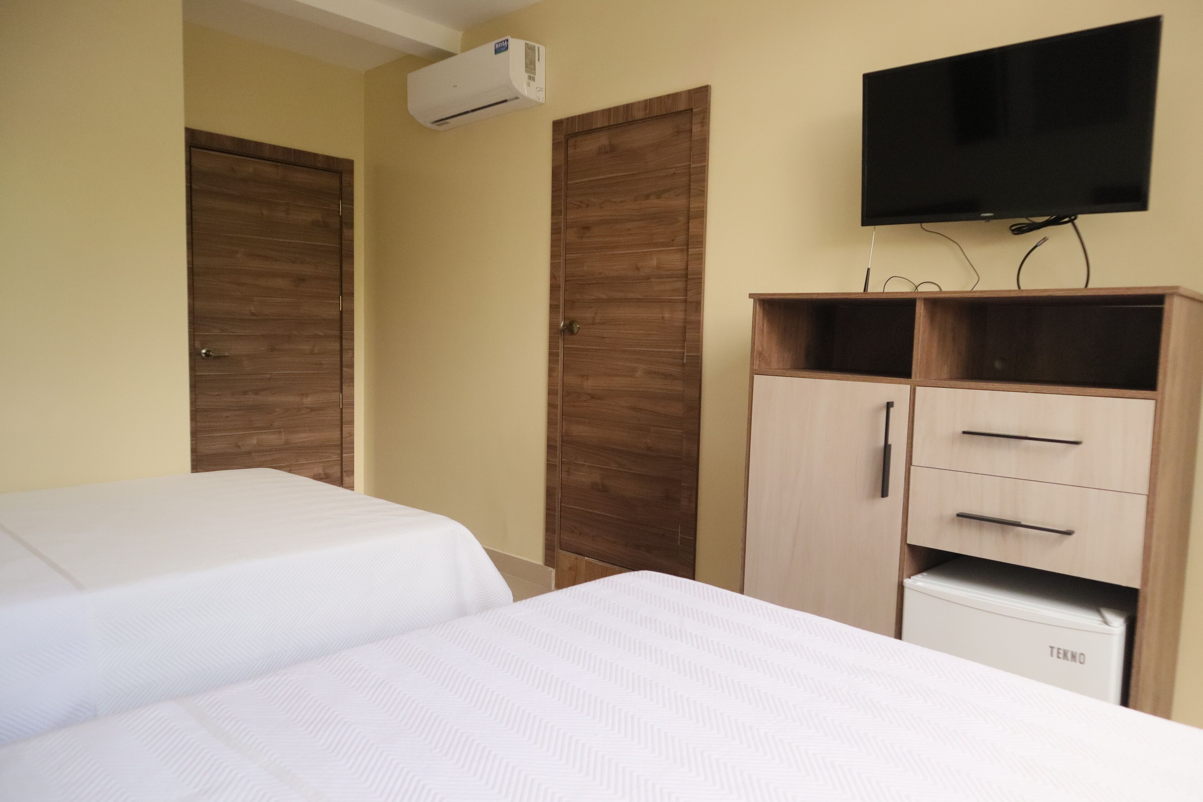 A hotel room with two beds, wooden wardrobes, a TV, and a minibar.