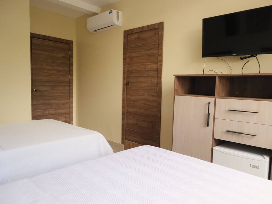 A hotel room with two beds, wooden wardrobes, a TV, and a minibar.