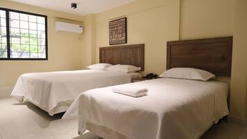 Two single beds with wooden headboards, a window with a view of greenery, and an air conditioning unit on the wall.