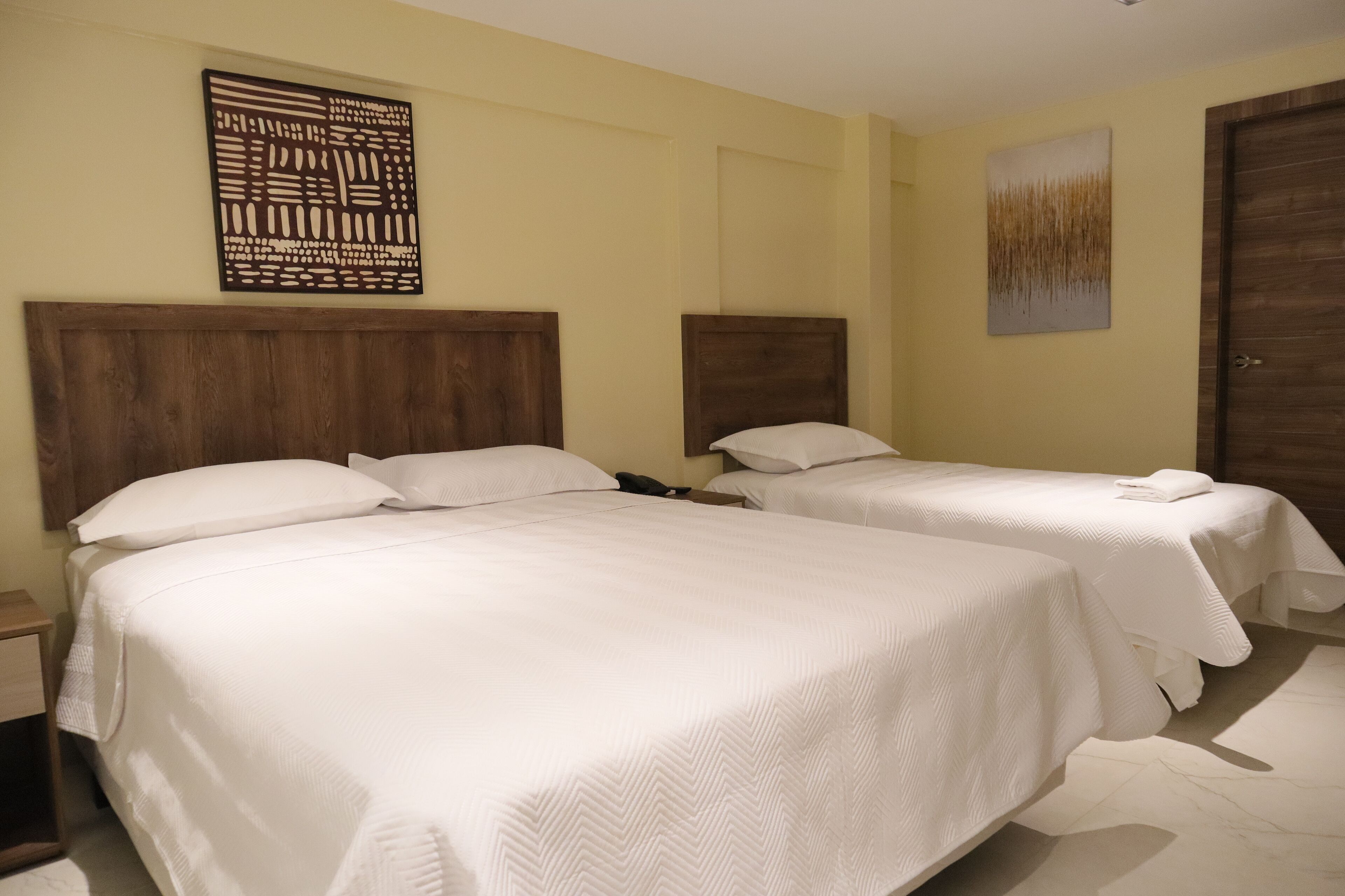 A hotel room with two beds, wooden headboards, and a large abstract artwork on the wall.