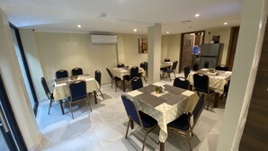 A dining area with multiple tables and chairs, an air conditioning unit, and a refrigerator in the background. - Hotel Sada (Guayaquil)