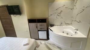 A hotel room with a bed, a built-in bathtub, a wardrobe, and a flat-screen TV mounted on the wall. - Hotel Sada (Guayaquil)