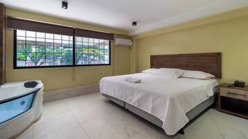 A hotel room with a bed, a small bedside table with a phone, a window with a view of buildings and trees, and a bathtub.