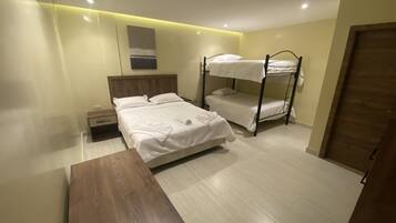 A bedroom with a bunk bed, a single bed, a wooden table, and a nightstand.
