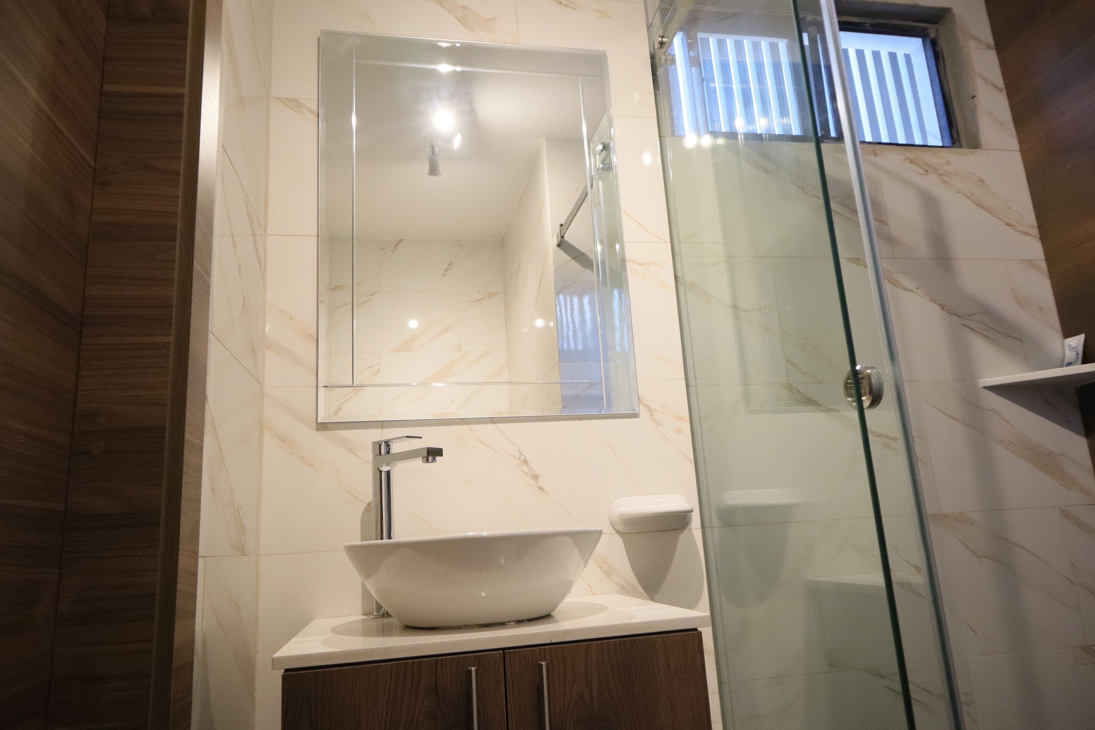 Un baño con ducha envuelta en vidrio, un lavabo blanco tipo recipiente y un espejo sobre el lavabo.