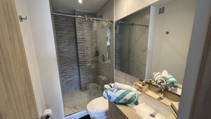 Une salle de bain moderne avec une douche à parois de verre, des toilettes et un lavabo surmonté d’un miroir.