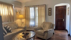 A living room with a sofa, armchair, and a glass coffee table. There is a lamp, curtains, and a door in the background. - Elegant house near Lake Michigan & Lambeau Field (Two Rivers)