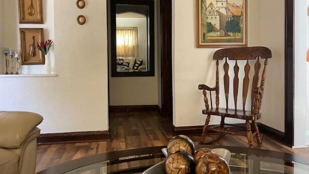 A living room with a wooden rocking chair, a glass coffee table with decorative items, a framed painting on the wall, and a mirror reflecting the room. - Elegant house near Lake Michigan & Lambeau Field (Two Rivers)