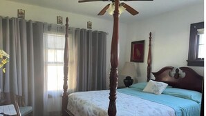 A four-poster bed with a floral bedspread, a wooden nightstand, and a window with curtains. - Elegant house near Lake Michigan & Lambeau Field (Two Rivers)