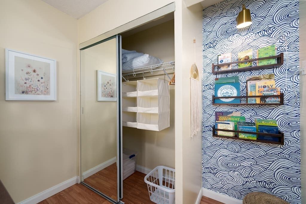 Ein Zimmer mit einer Schiebetür zum Kleiderschrank, einem weißen Wäschekorb und einer Wand mit ornamentalem Wandpapier.