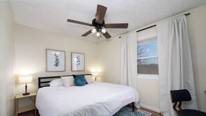 A bedroom with a bed, two bedside lamps, a ceiling fan, a window with curtains, and a chair. - NEW! ARK Family Retreat w/ Game Room 3min to Ark! (Williamstown)